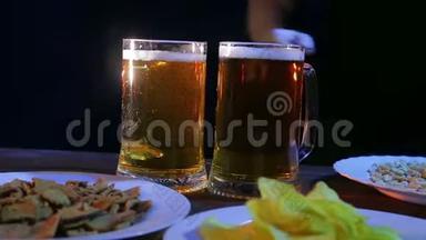 酒保在桌子上放着黑色背景上的零食，两杯满是泡沫的啤酒